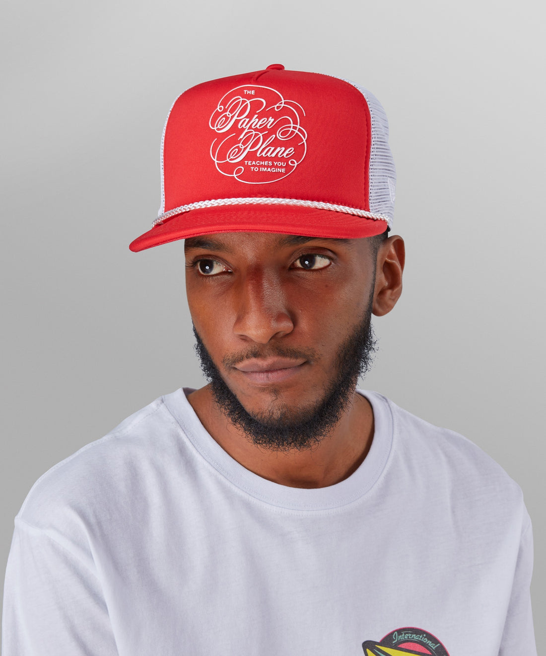 CUSTOM_ALT_TEXT:Male model wearing Paper Planes Script Trucker Hat color Coral Red.