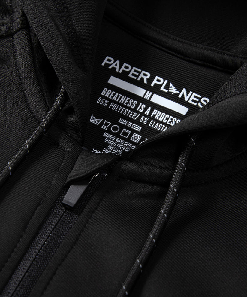 CUSTOM_ALT_TEXT: Neck opening detail with reflective drawcord on Paper Planes Greatness Is a Process Zip-Up Hoodie, color Black.